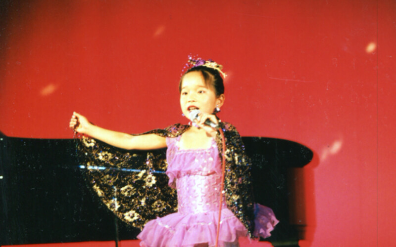 9歳の頃、発表会のステージで歌を歌う川島あいさん